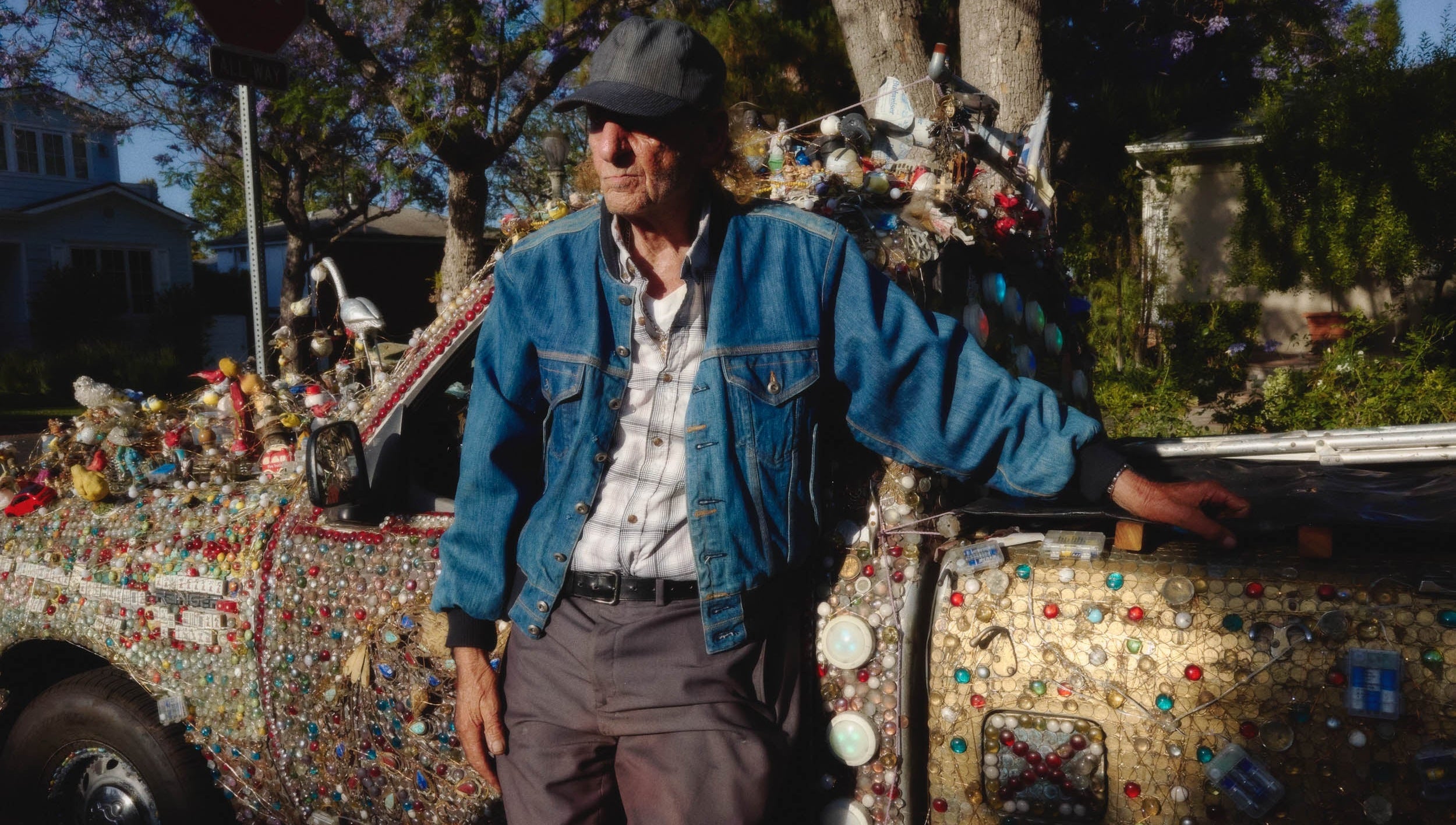Man standing next to a colorful, decorated vehicle with a house and trees in the background