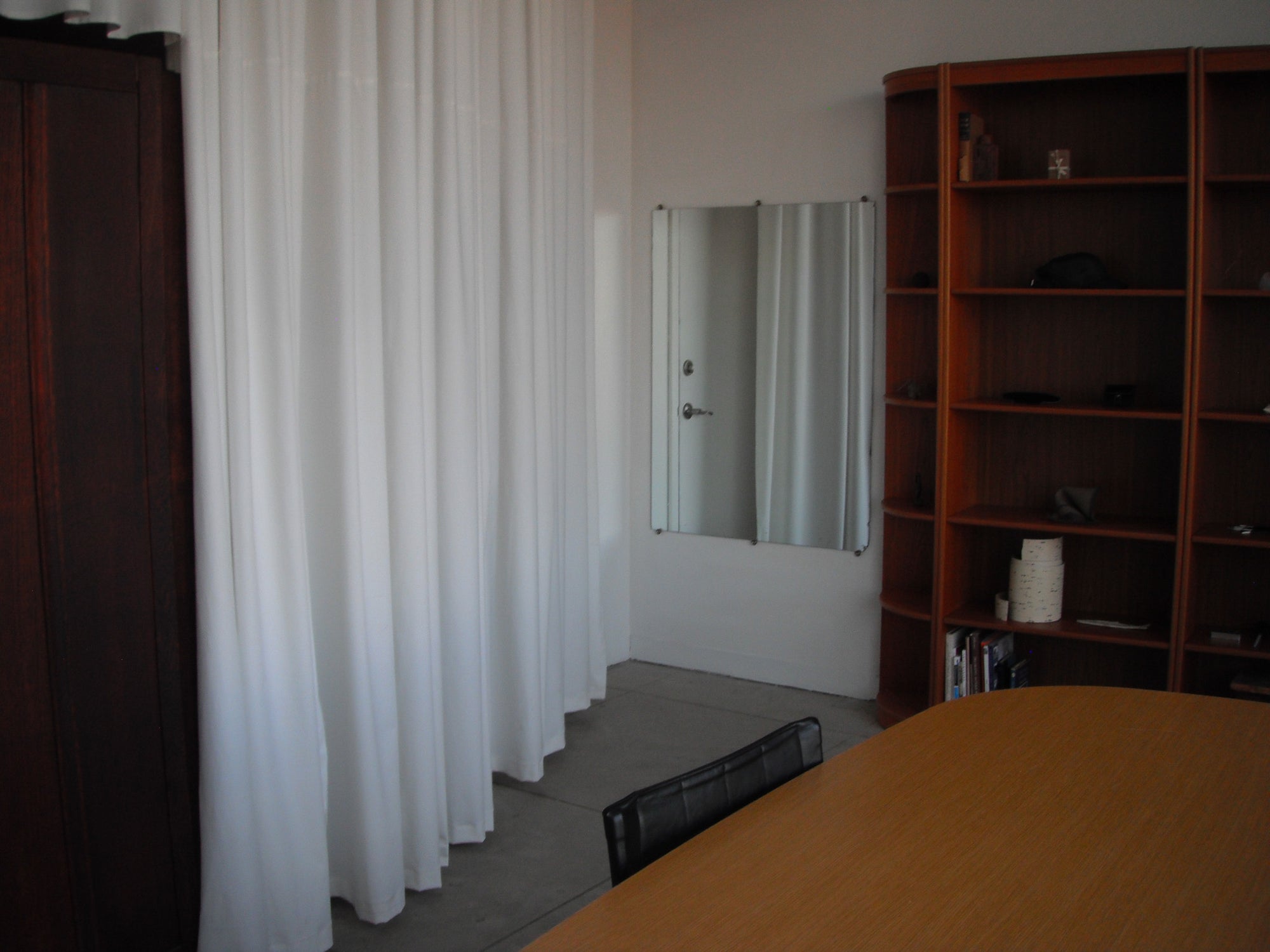 Object from Nothing Showroom with a table, bookshelf, and mirror reflecting a door.