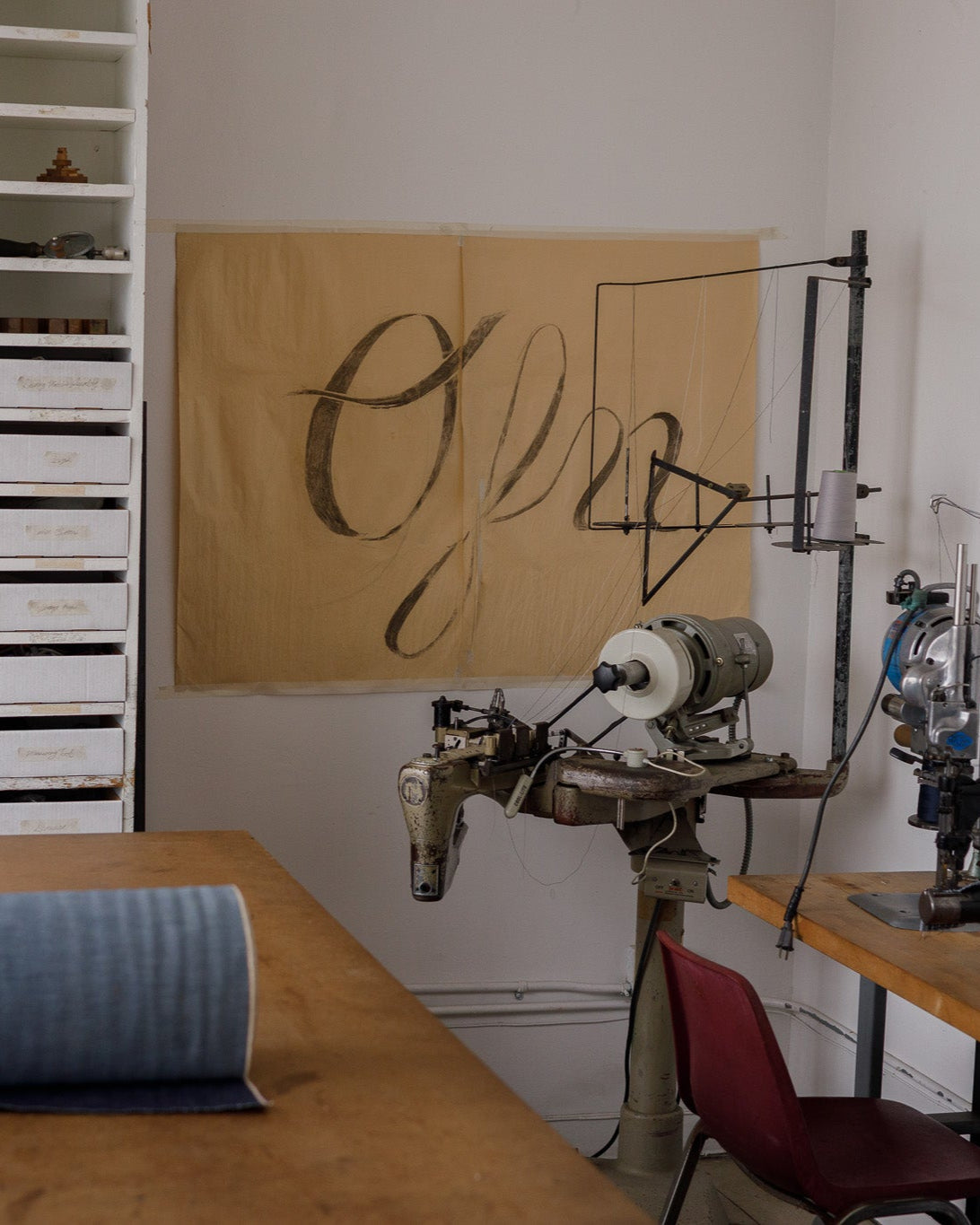 Interior of Object From Nothing's upcycling studio with vintage sewing equipment, denim roll, and hand-painted banner, showcasing sustainable garment production
